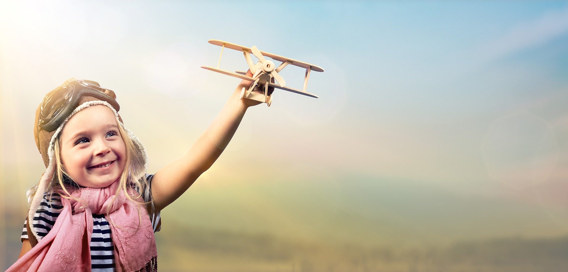 Kind spielt draußen fröhlich mit Holzflugzeug, es wirkt ausgelassen und glücklich